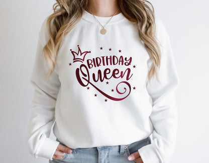 A woman wearing a white sweatshirt with a graphic design that says "Birthday Queen" and stars.