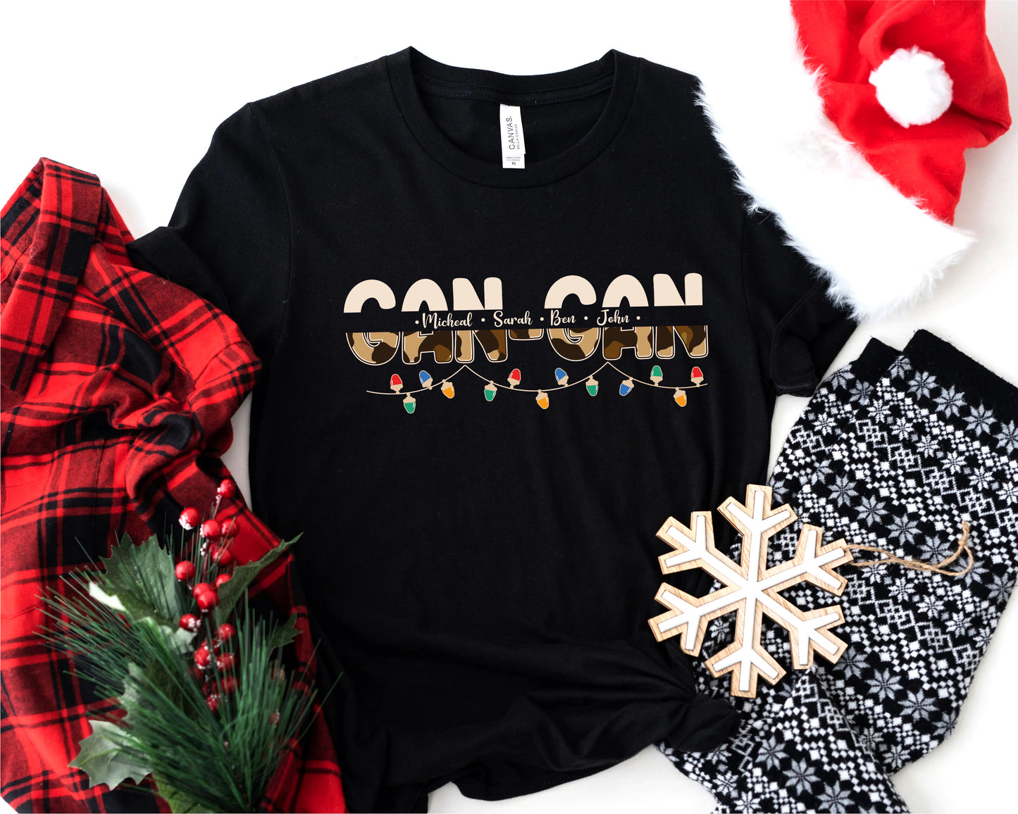 A black t-shirt with a Christmas-themed design, including a snowflake, lights, and text, along with a Santa hat and a red plaid shirt.