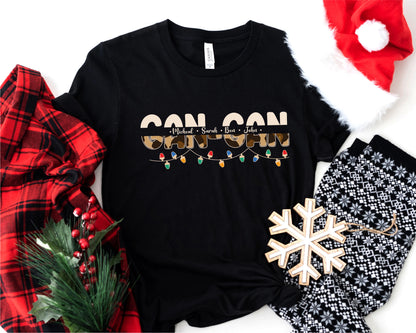 A black t-shirt with a Christmas-themed design, including a snowflake, lights, and text, along with a Santa hat and a red plaid shirt.