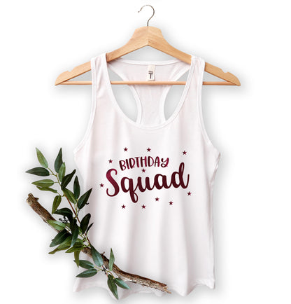 A white tank top with the text "Birthday Squad" printed on it, hanging on a wooden hanger.
