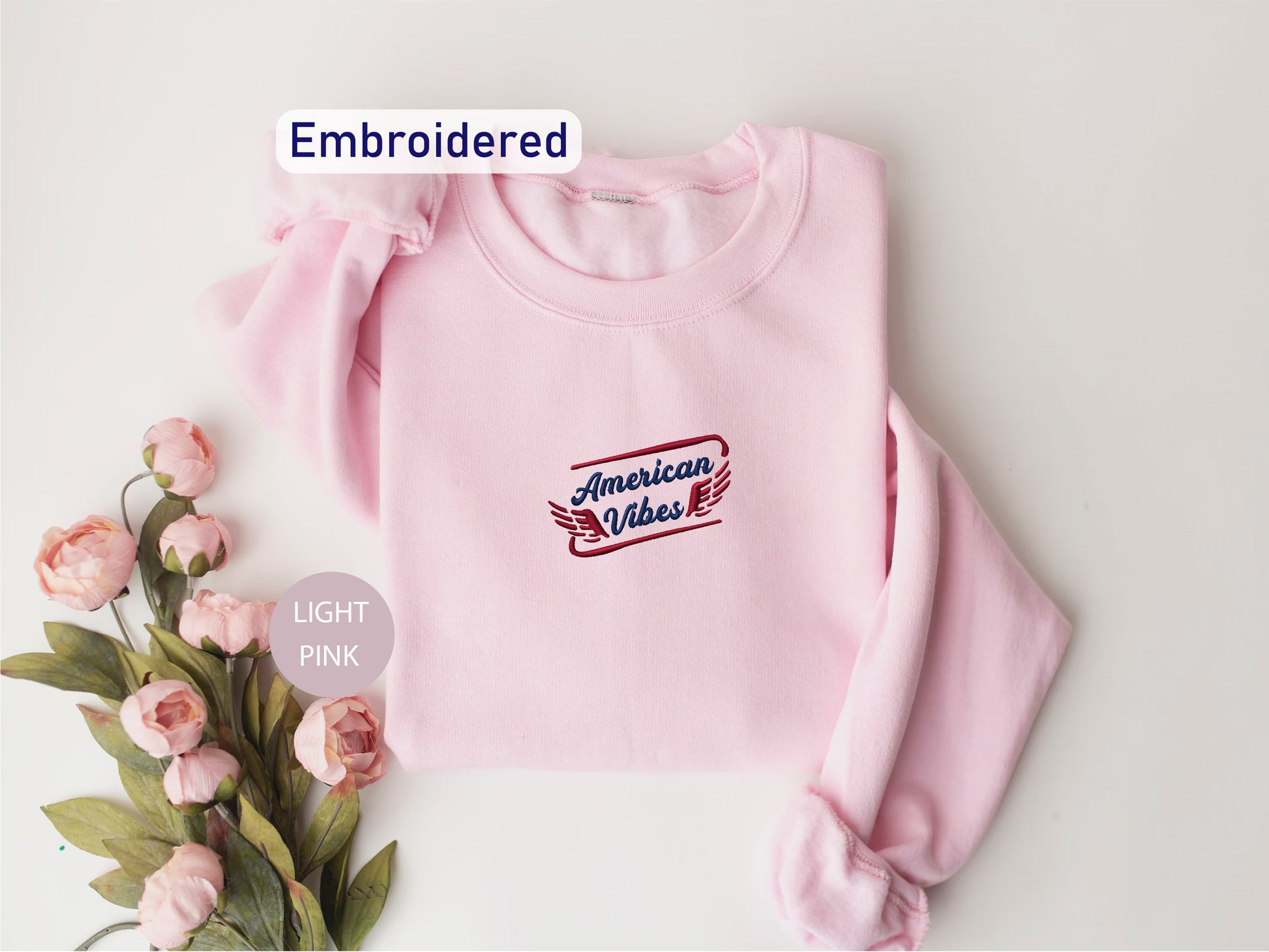 a pink sweatshirt with an embroidered design, placed on a white background alongside a bouquet of pink flowers.