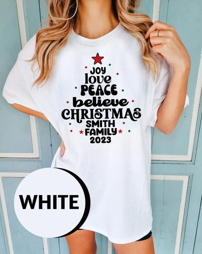 A woman wearing a white t-shirt with a Christmas tree design and text printed on it.