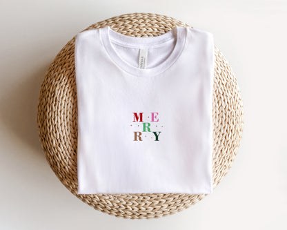 A white t-shirt with the word "MERRY" printed on it, laid out on a woven basket or mat.