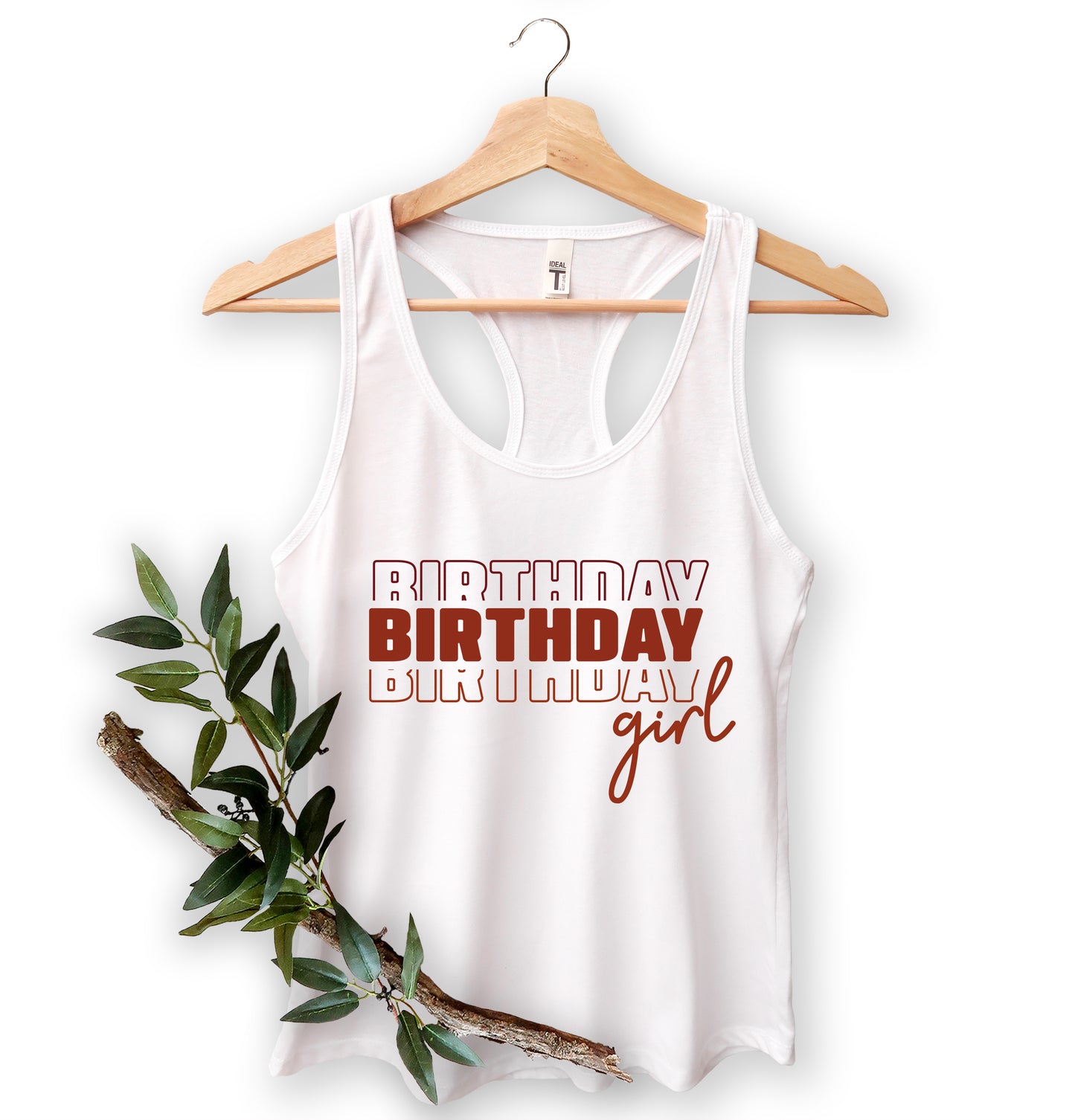 A white tank top with the text "BIRTHDAY BIRTHDAY girl" printed on it, hanging on a wooden hanger.