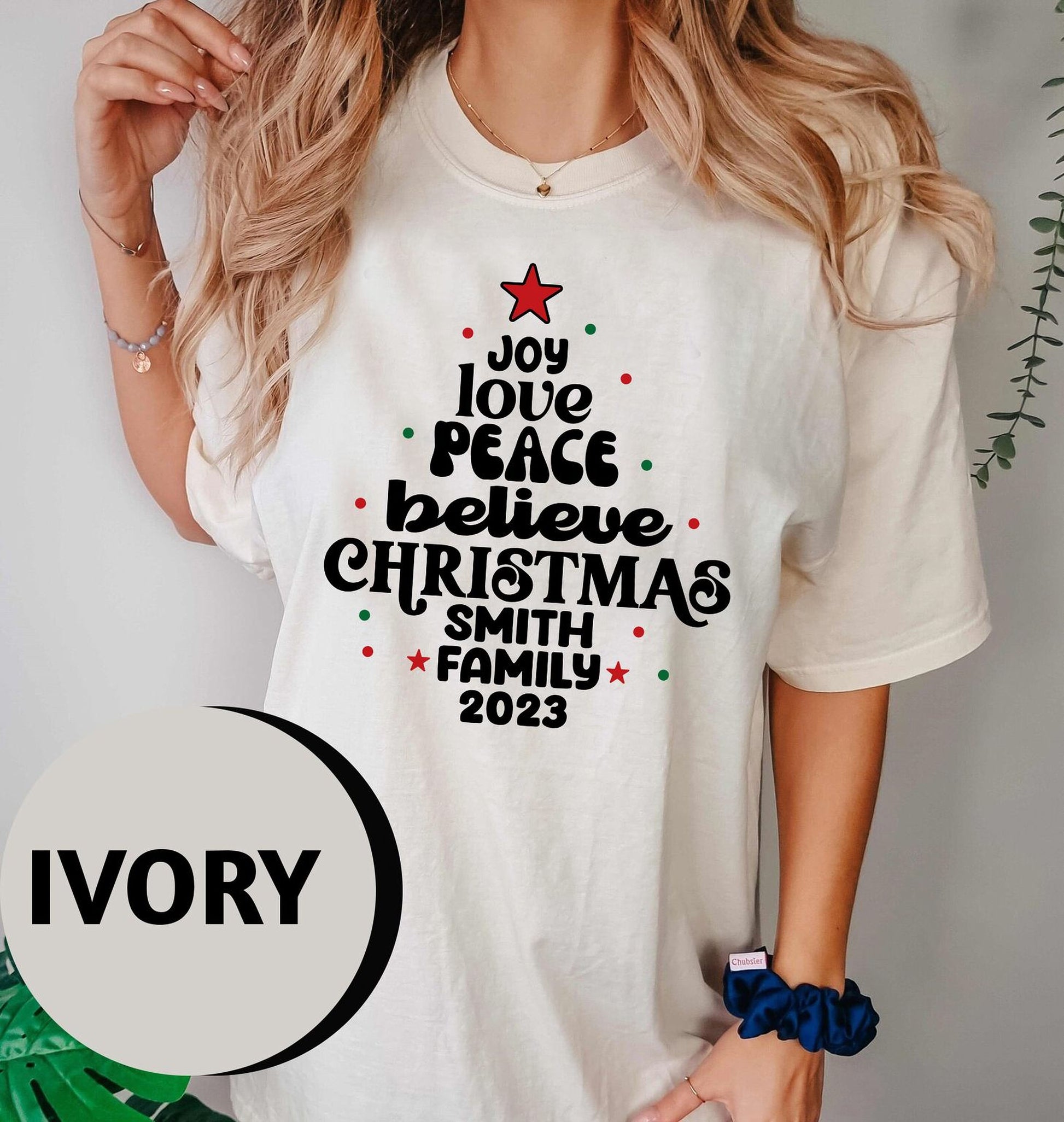 A woman wearing a white t-shirt with a Christmas tree design and text printed on it.