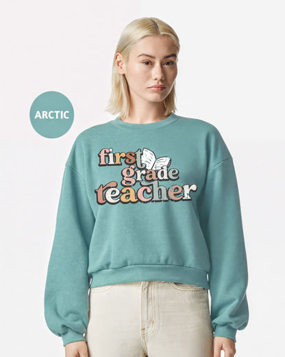 A woman wearing a teal sweatshirt with the text "first grade teacher" printed on it.