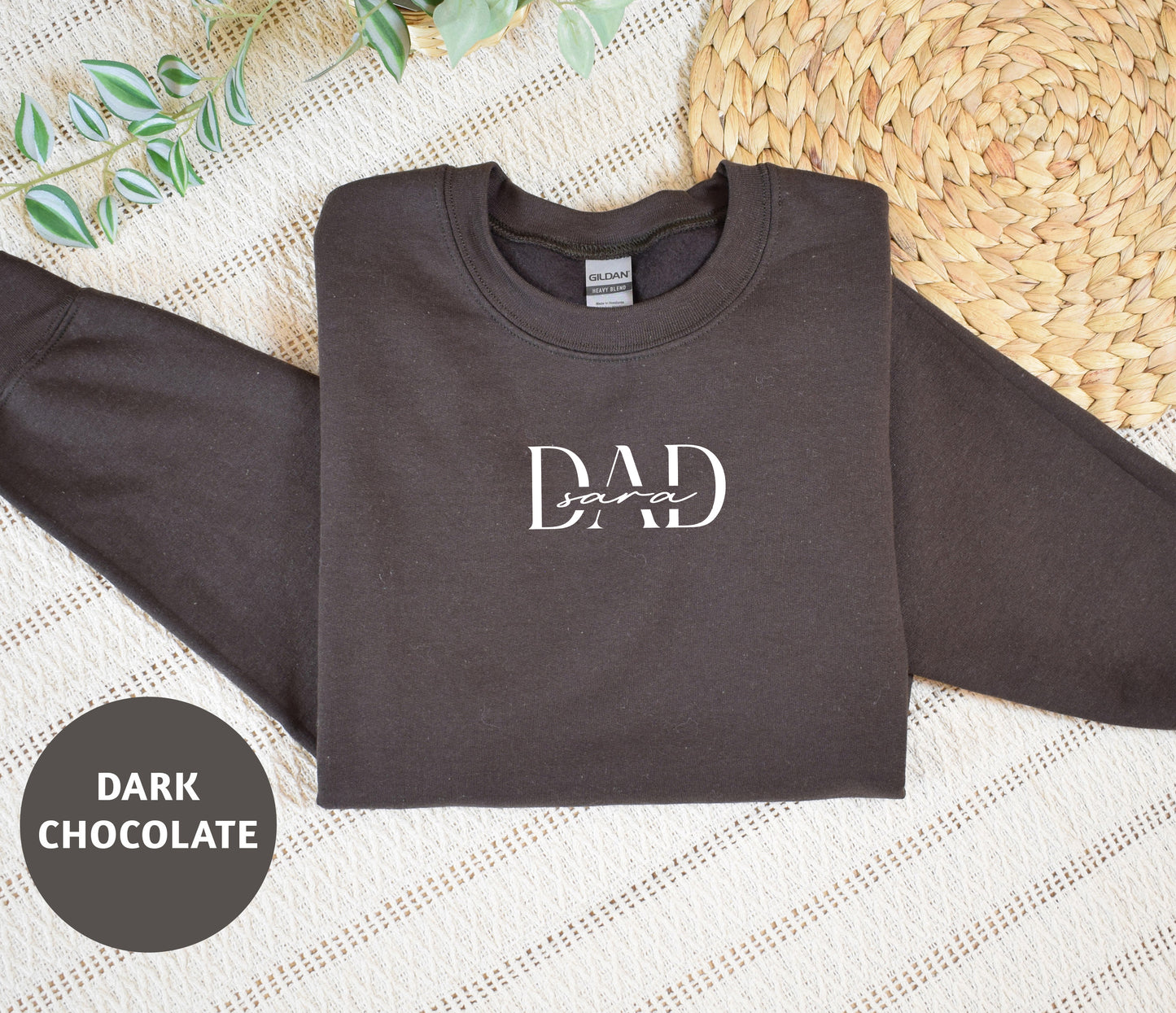 A dark grey sweatshirt with the text "DAD soar" printed on it, along with a straw mat and some greenery in the background.