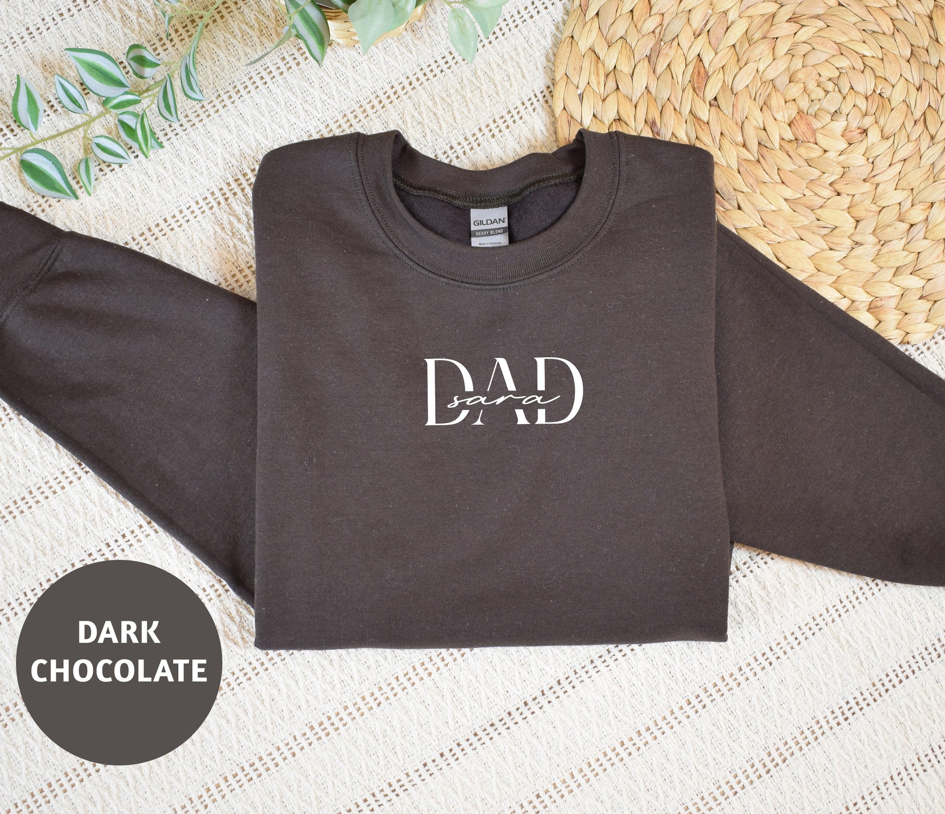 A dark grey sweatshirt with the text "DAD soar" printed on it, along with a straw mat and some greenery in the background.
