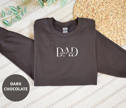 A dark grey sweatshirt with the text "DAD soar" printed on it, along with a straw mat and some greenery in the background.