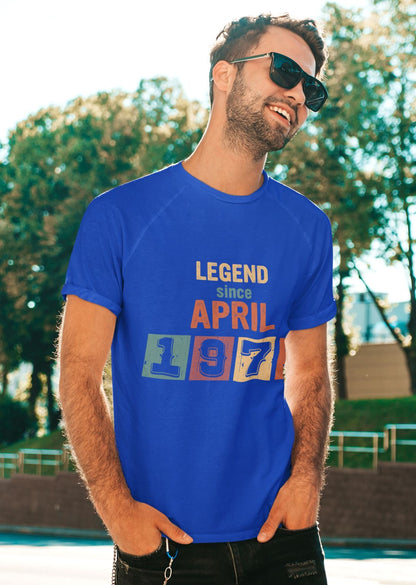 A man wearing a blue t-shirt with the text "LEGEND since APRIL 1877" is smiling and standing outdoors in front of a natural background.