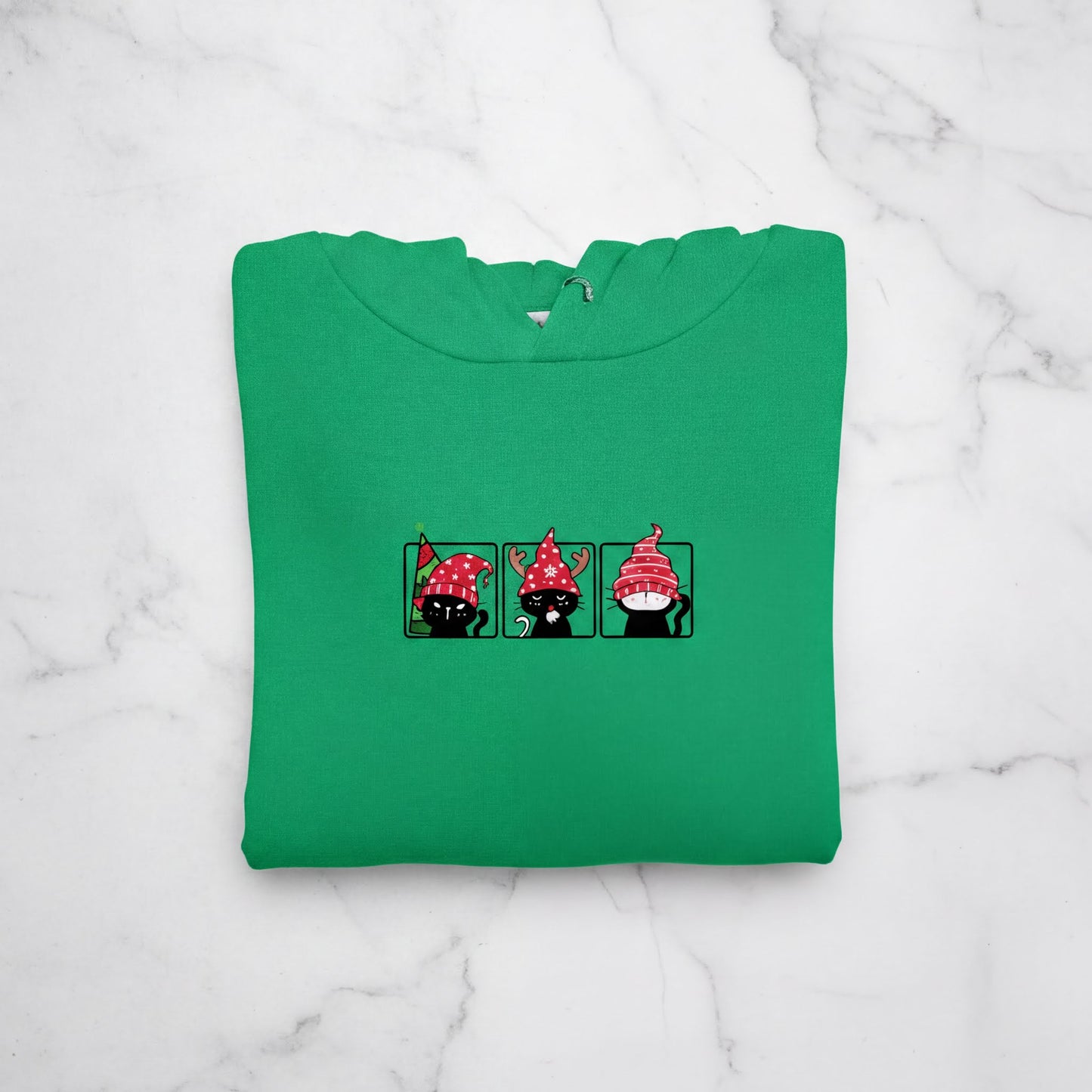 A green hoodie with a graphic design of three cartoon cats wearing red hats.