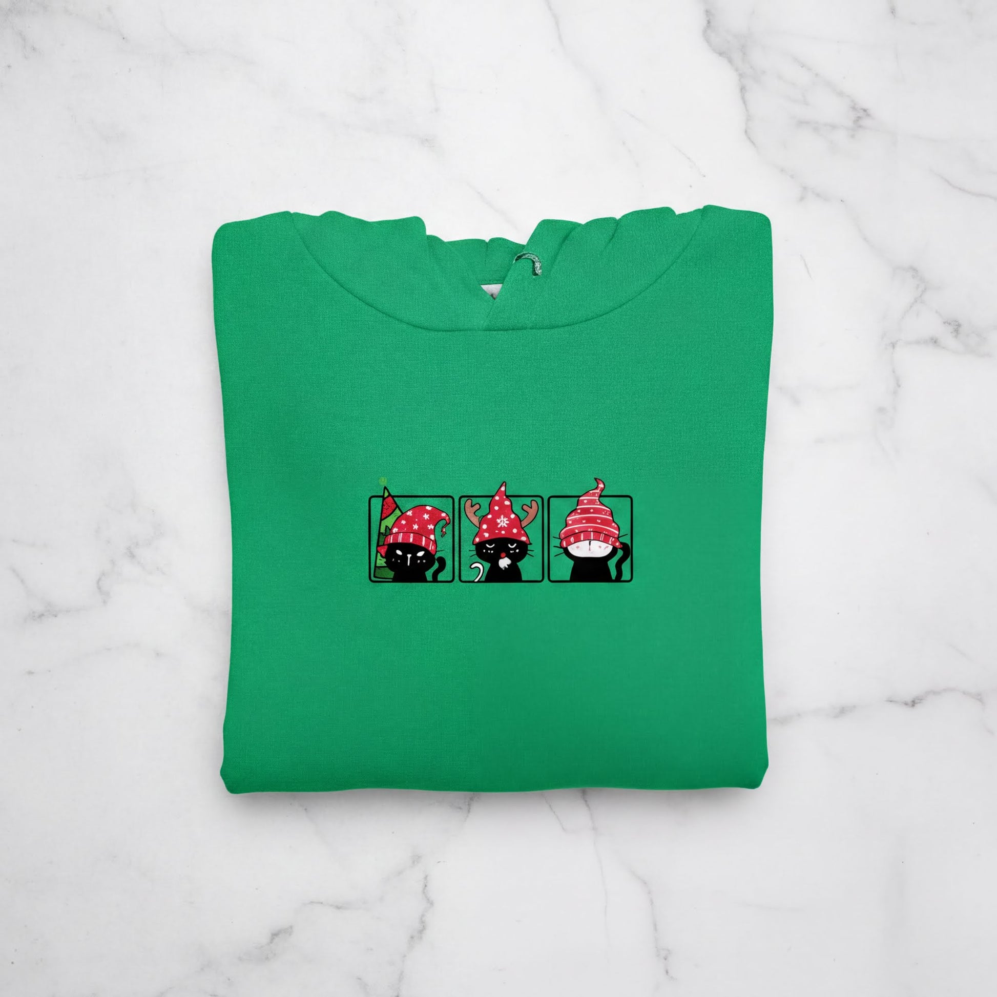 A green hoodie with a graphic design of three cartoon cats wearing red hats.