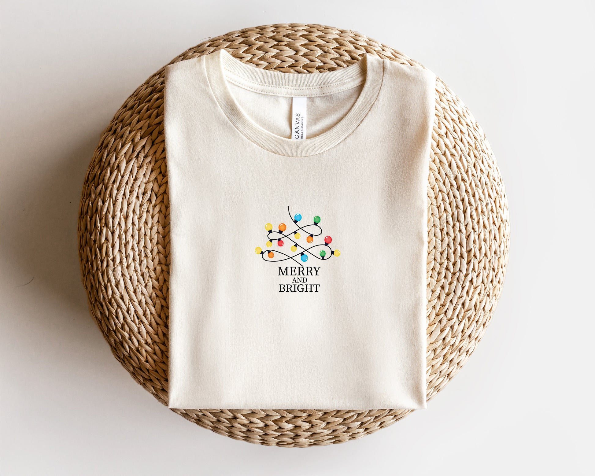 A white t-shirt with a colorful graphic design and text printed on it, placed on a woven mat.