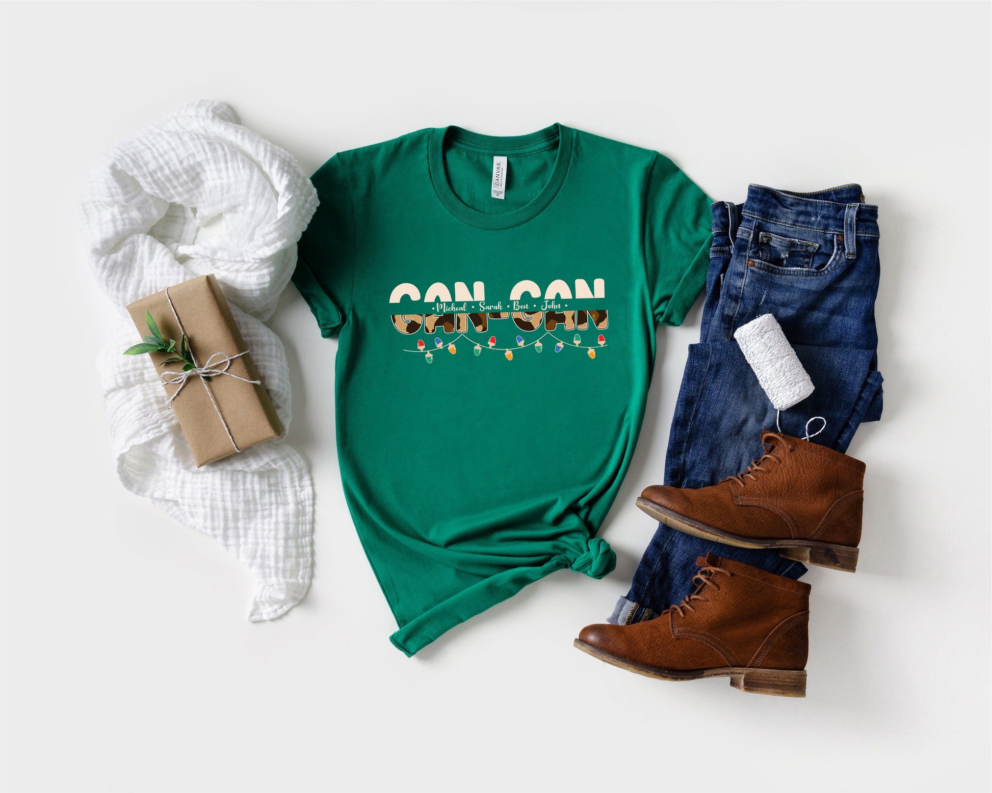 A green t-shirt with a graphic design, a pair of jeans, a pair of brown boots, and a wrapped gift box are arranged on a white background.