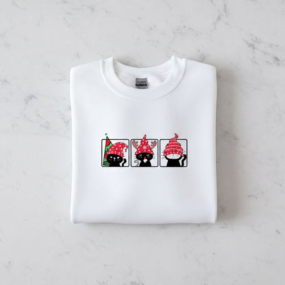 A white t-shirt with a graphic design of three cats wearing festive hats, including a Christmas-themed hat.