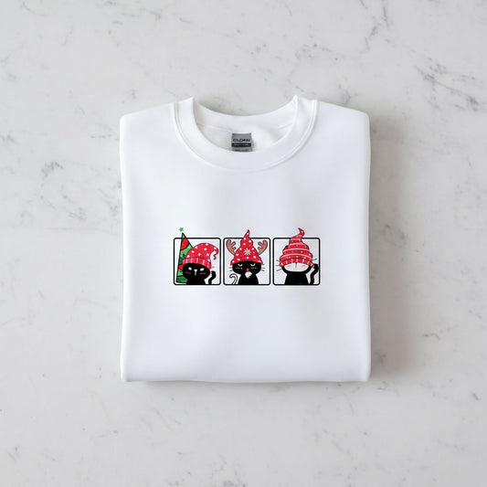 A white t-shirt with a graphic design of three cats wearing festive hats, including a Christmas-themed hat.