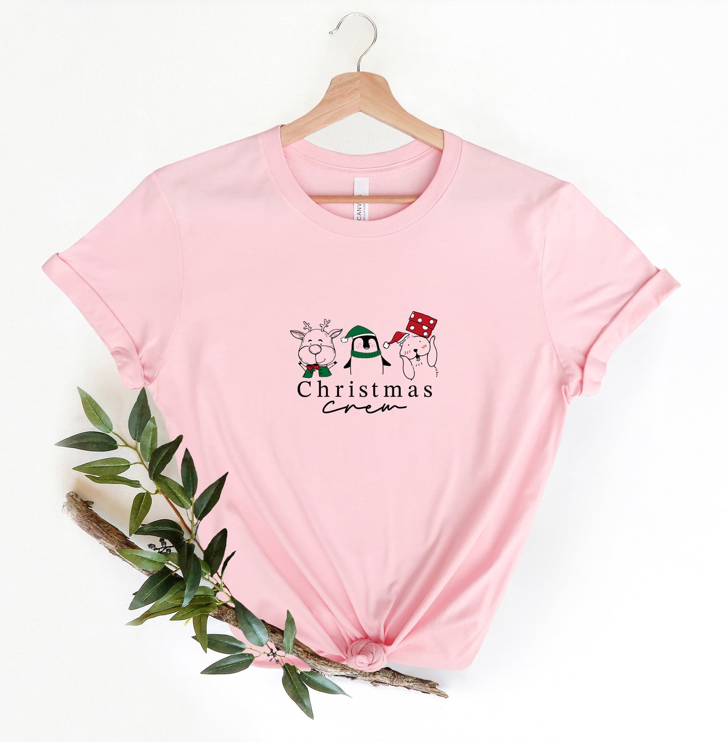 A pink t-shirt with a Christmas-themed graphic design, including a reindeer, a penguin, and a snowman, along with the text "Christmas" printed on it.