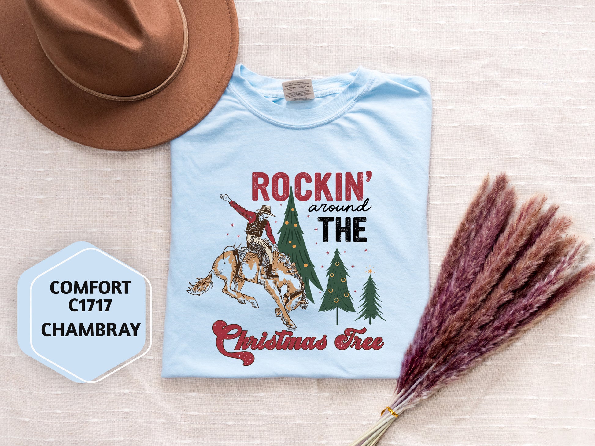 a light blue t-shirt with a graphic design, a brown hat, and some pom pom flowers on a white background.