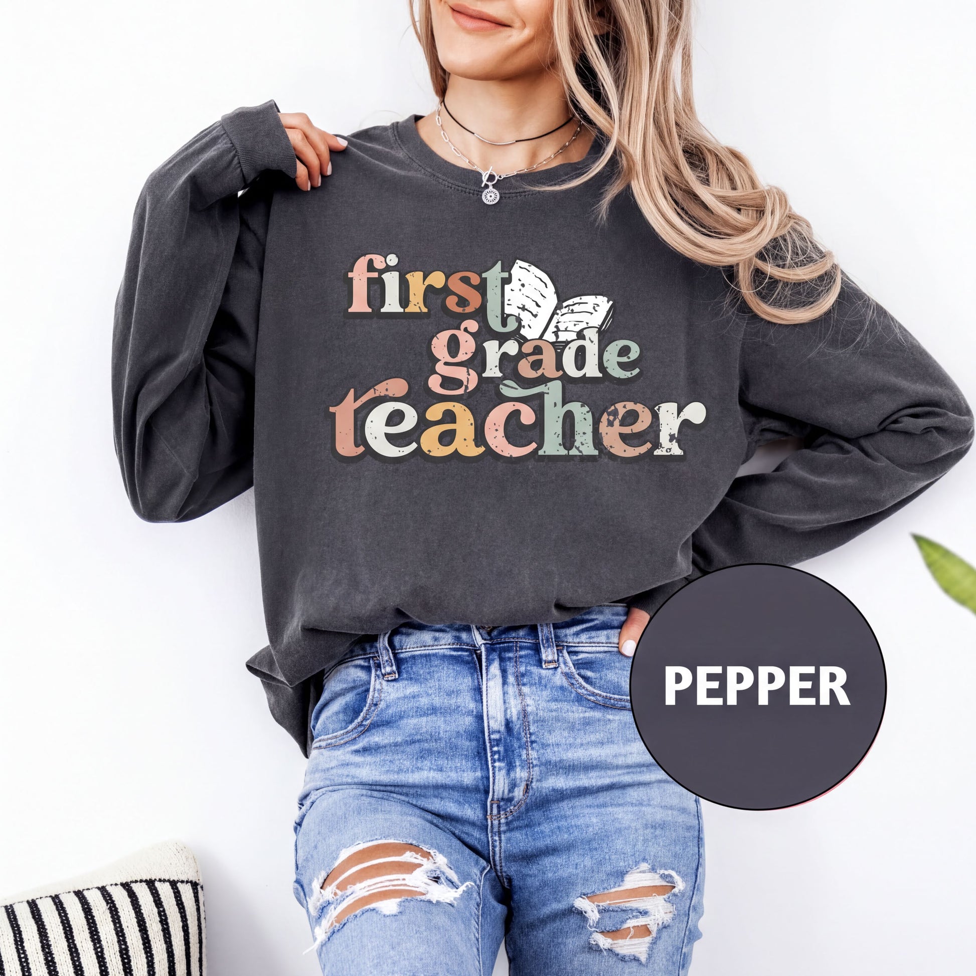 A woman wearing a black sweatshirt with the text "first grade teacher" printed on it, standing against a white background.