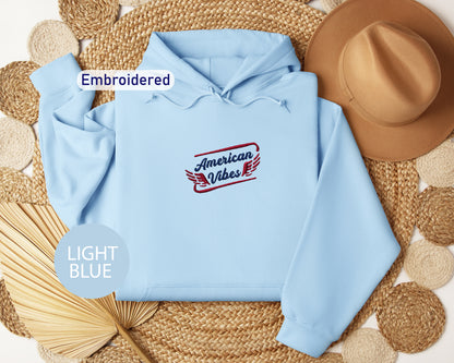 a light blue hoodie with an embroidered design, a brown hat, and a straw hat, all arranged on a woven mat.