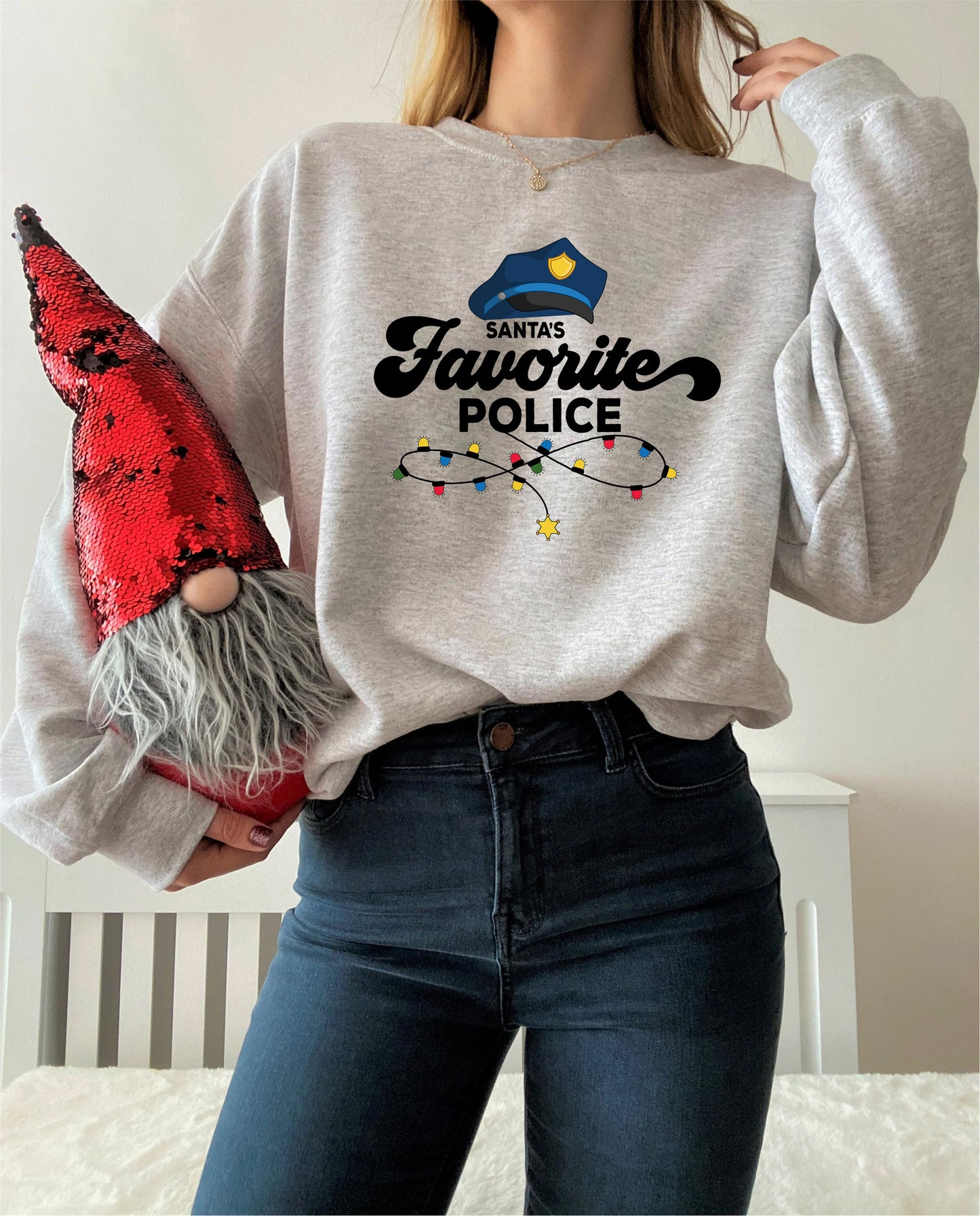 A woman wearing a gray sweatshirt with a graphic design and holding a red sequined gnome.