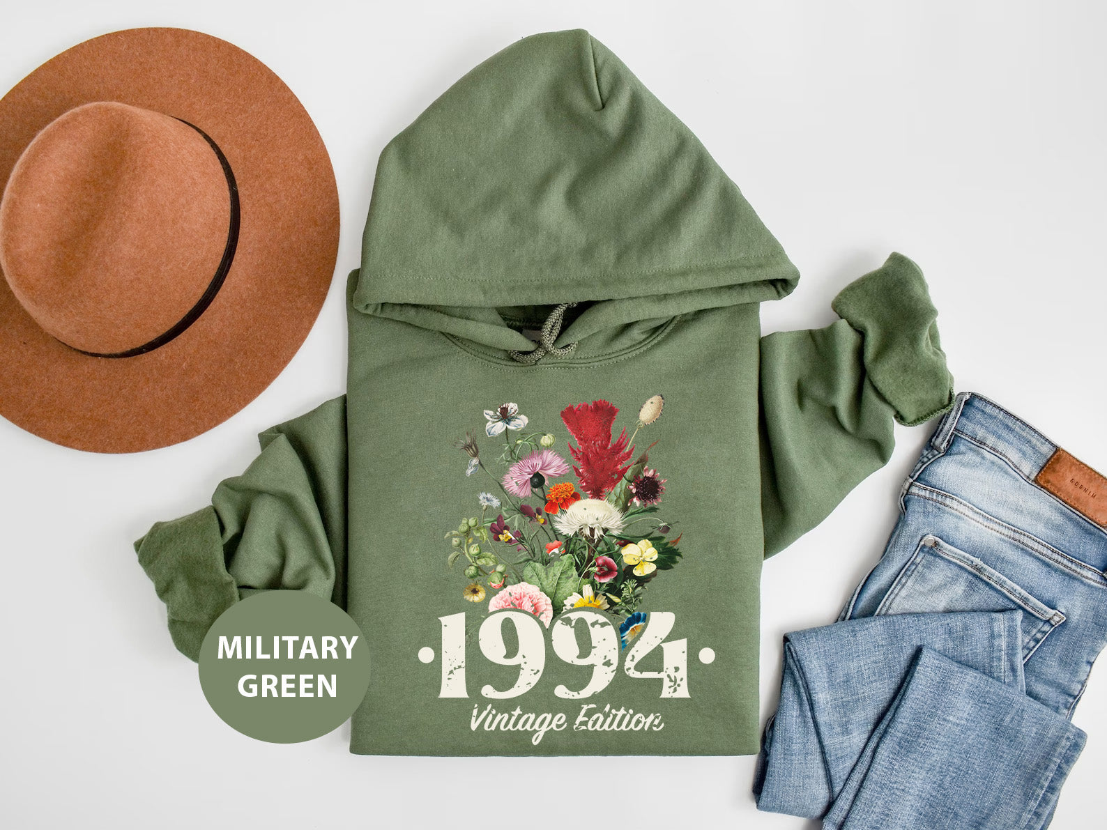 a green hoodie with flowers and a hat next to a pair of jeans