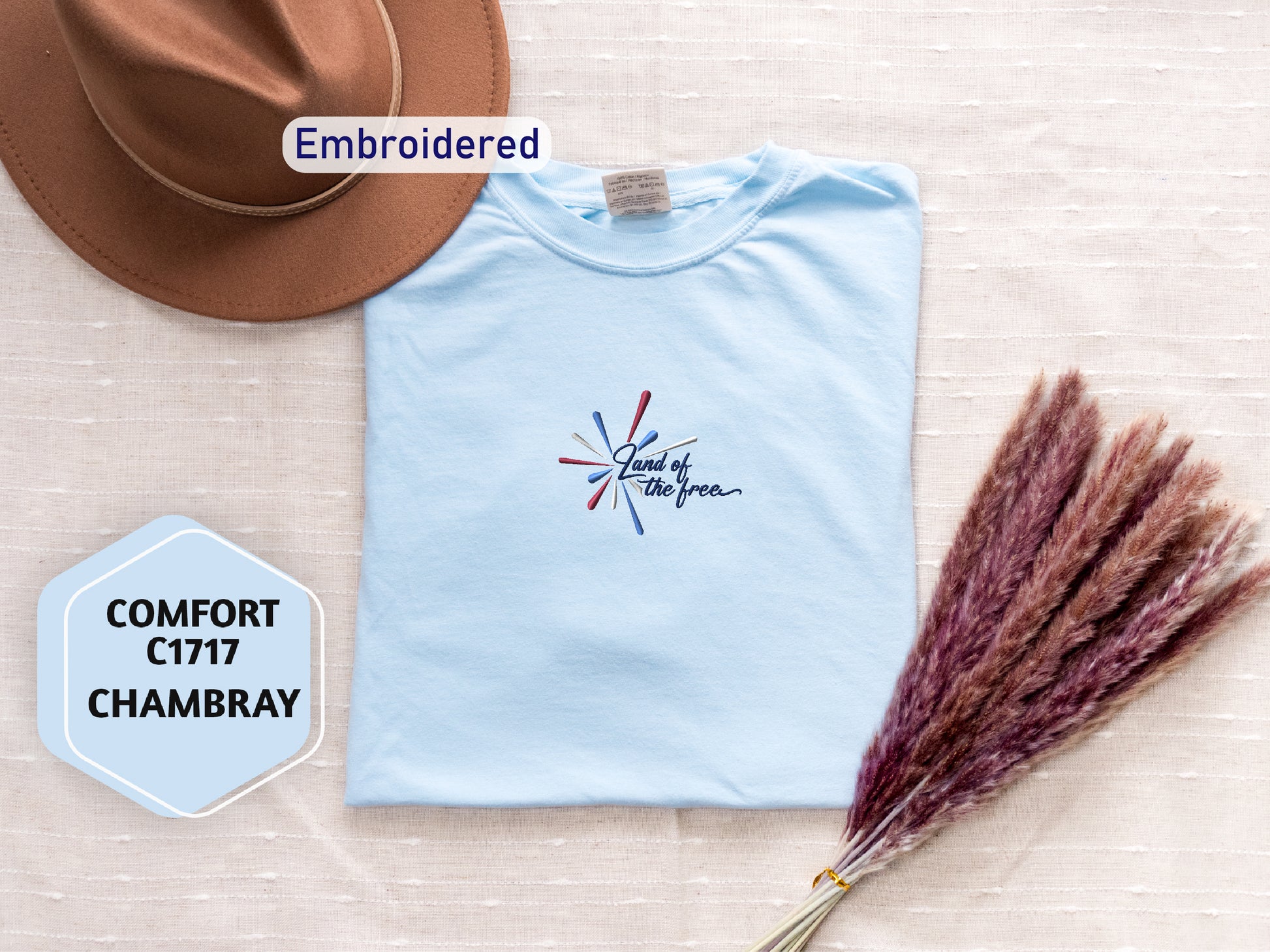a light blue t-shirt with a patriotic design, a brown hat, and a bunch of red and brown flowers, all arranged on a beige background.