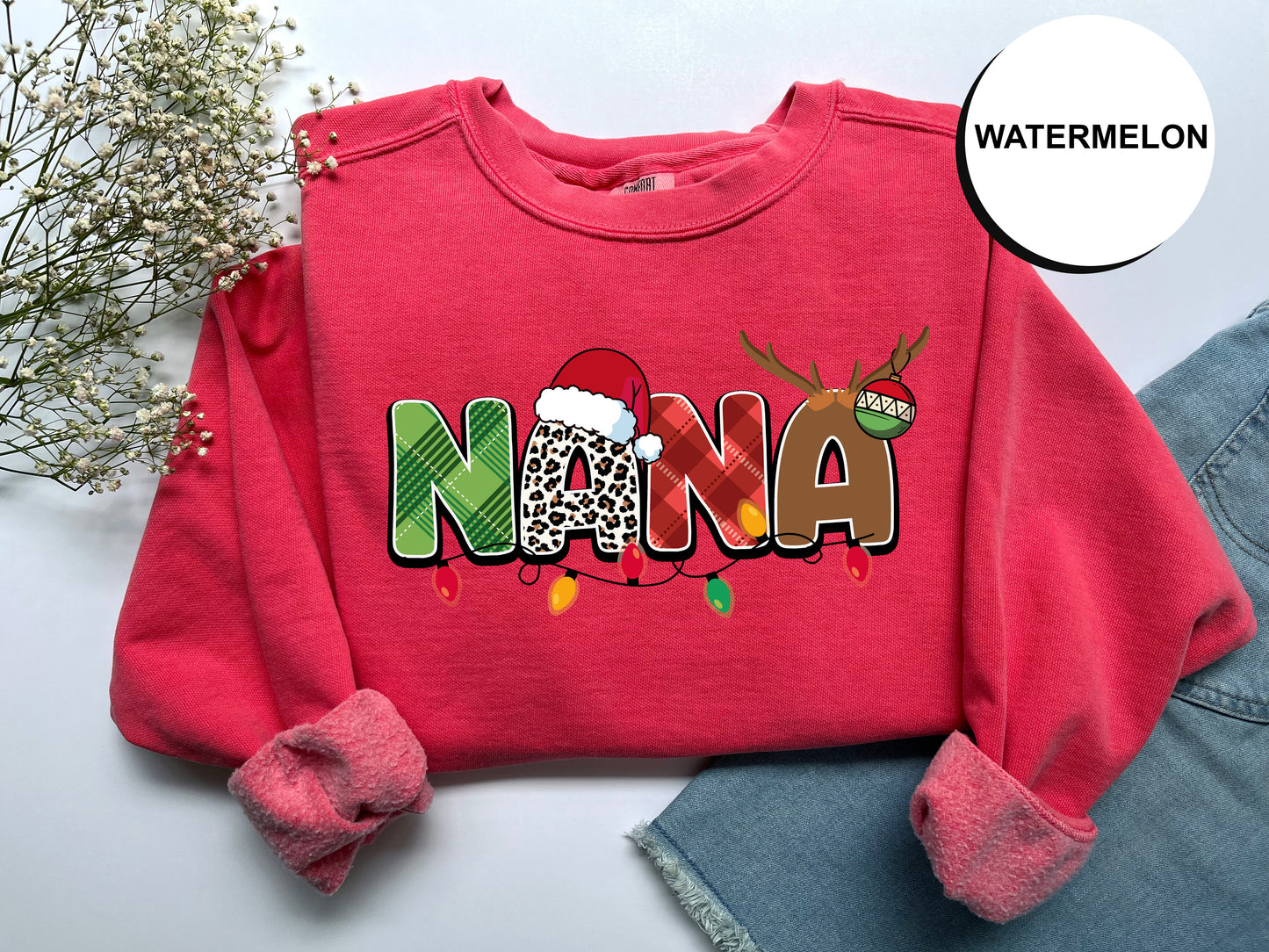 A red sweater with the word "NANA" printed on it, along with a Santa hat and Christmas lights, is displayed on a white surface.