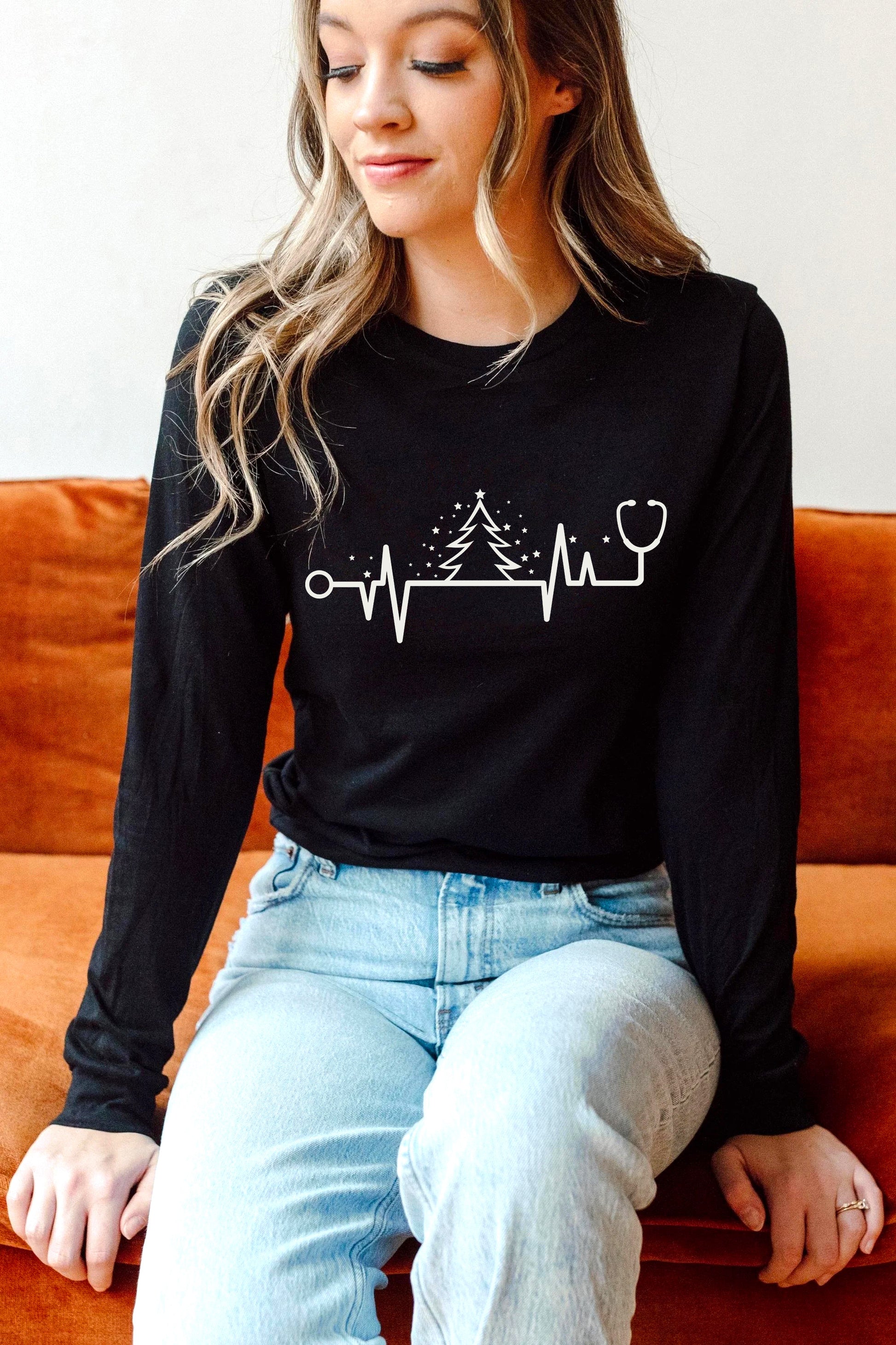 A woman wearing a black long-sleeved shirt with a white graphic design sits on an orange couch.