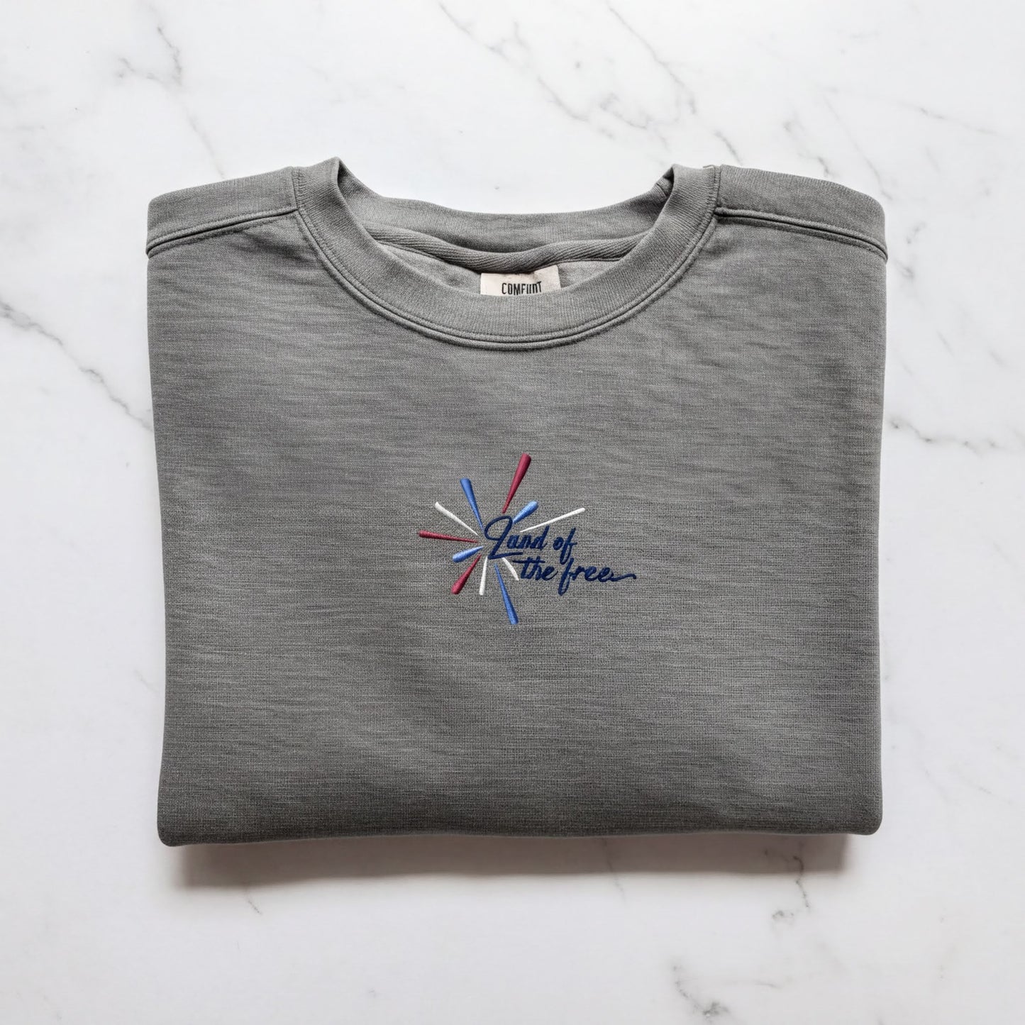 A gray sweatshirt with a blue and red embroidered design on the front, which says "Land of the free".