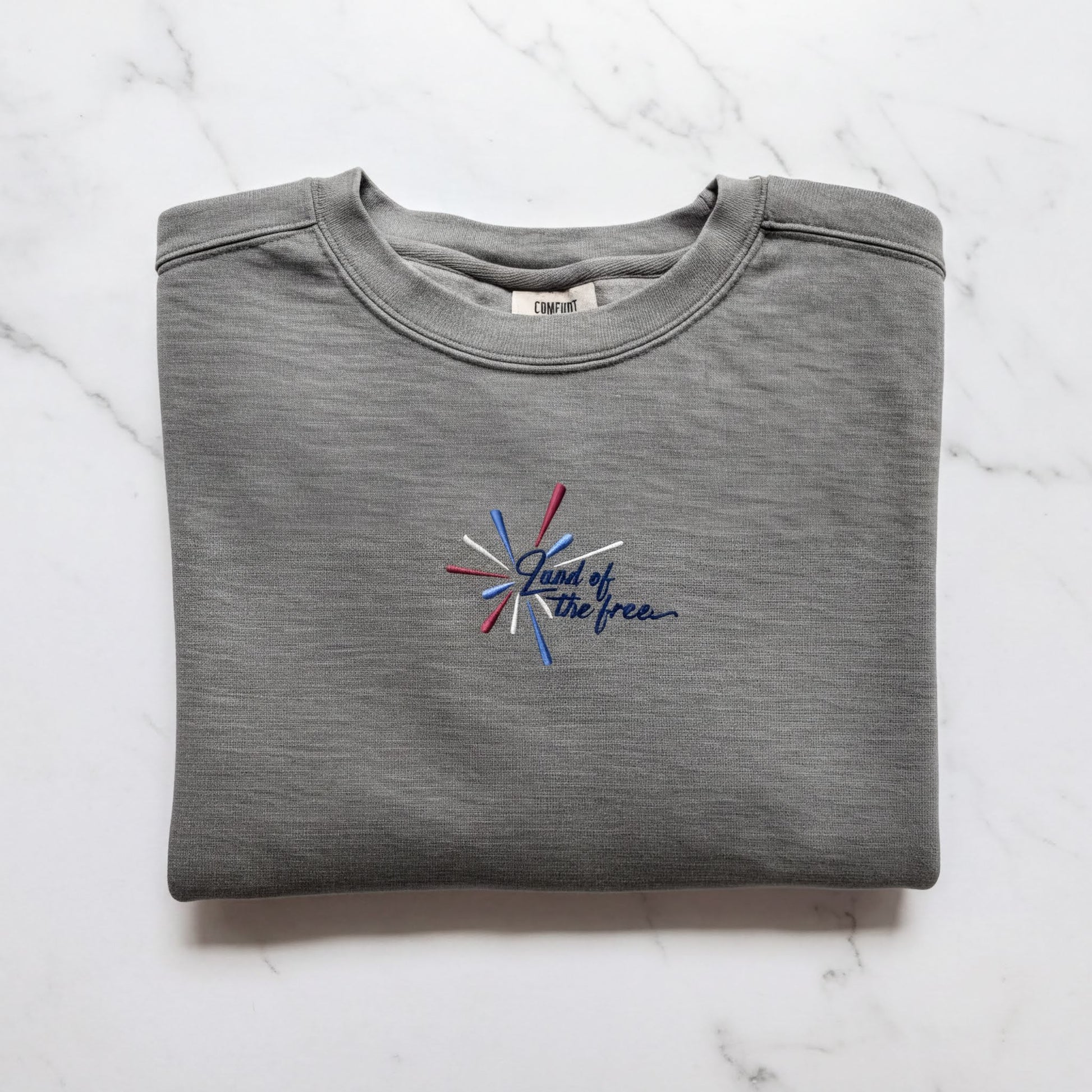 A gray sweatshirt with a blue and red embroidered design on the front, which says "Land of the free".