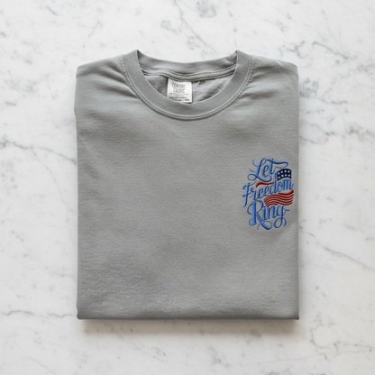 A gray t-shirt with a blue and red design on the left side, featuring the text "Let Freedom Ring" and an American flag.