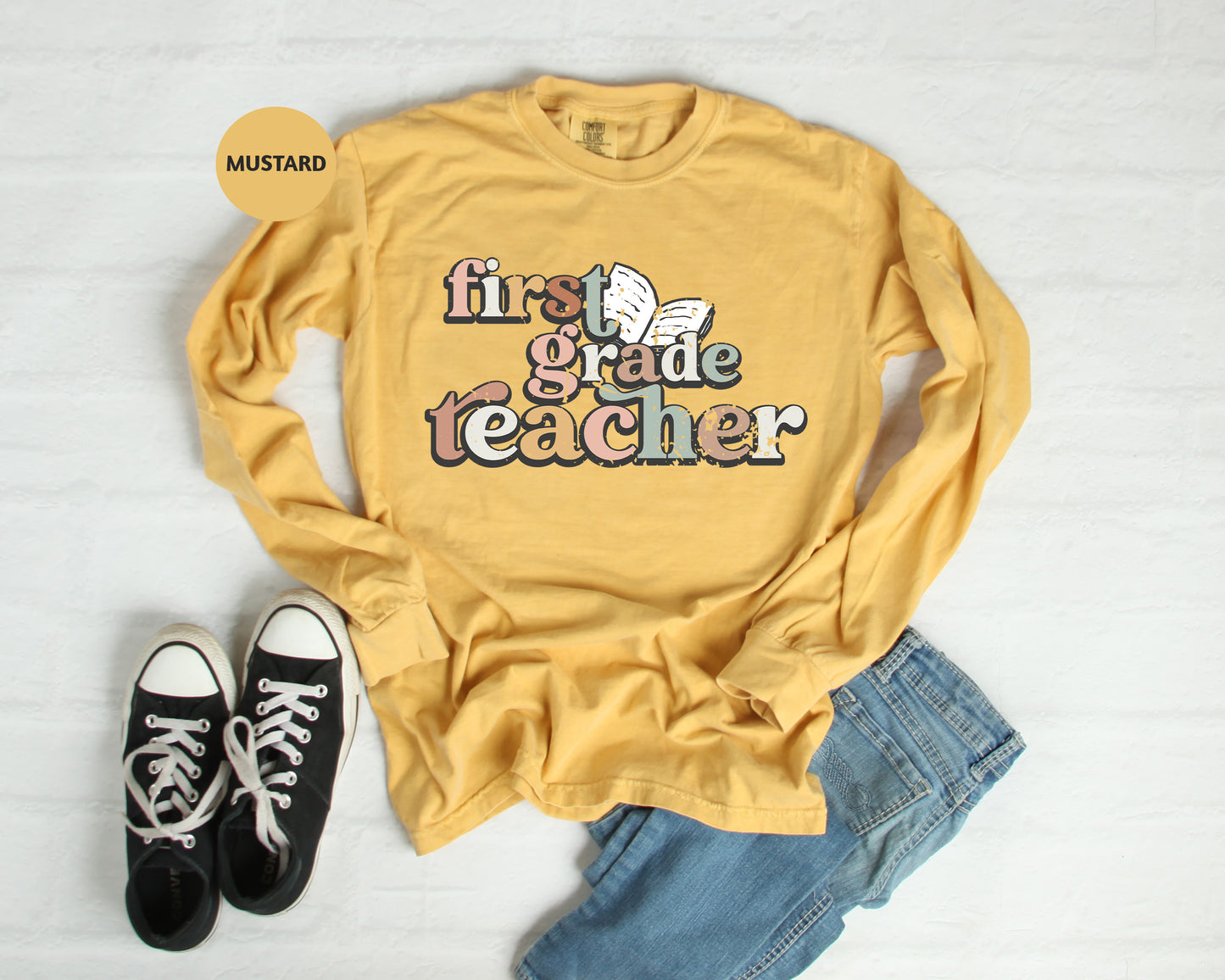 a yellow long-sleeved shirt with the text "first grade teacher" printed on it, along with a pair of black and white sneakers and blue jeans.