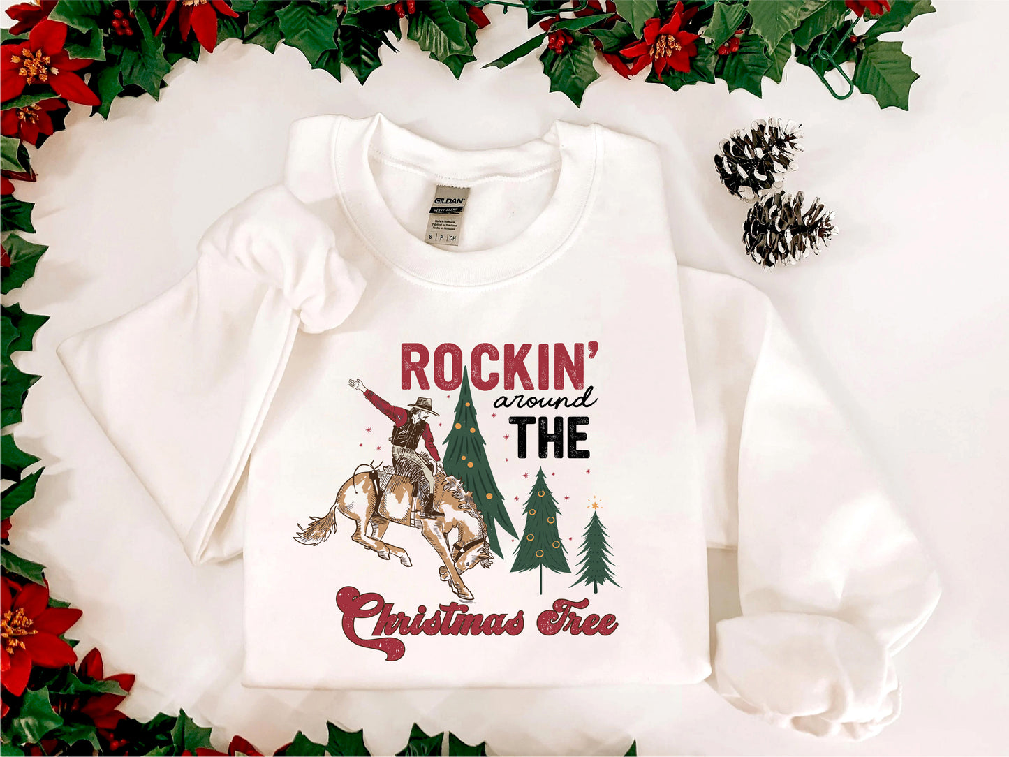A white t-shirt with a graphic design featuring a cowboy on a horse, surrounded by Christmas trees and pine cones, with the text "ROCKIN' around THE CHRISTMAS FREE" printed on it.