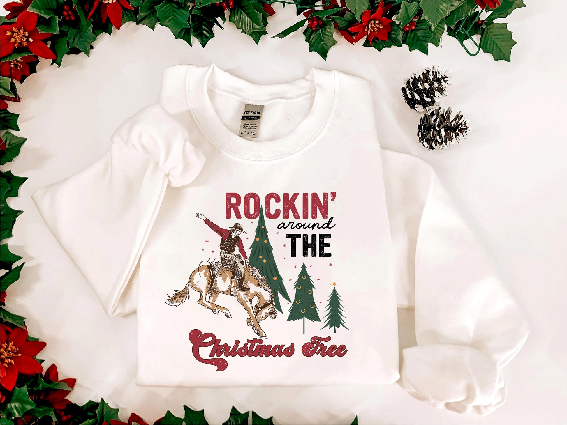 A white t-shirt with a graphic design featuring a cowboy on a horse, surrounded by Christmas trees and pine cones, with the text "ROCKIN' around THE CHRISTMAS FREE" printed on it.