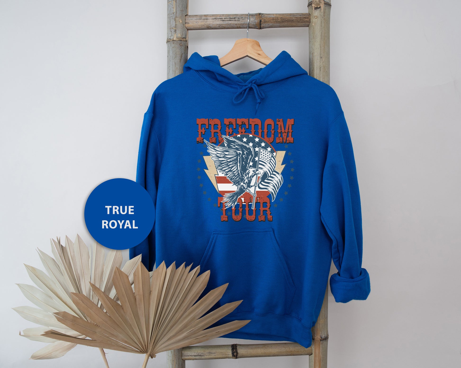 A blue hoodie with a graphic design and text, hanging on a wooden hanger.