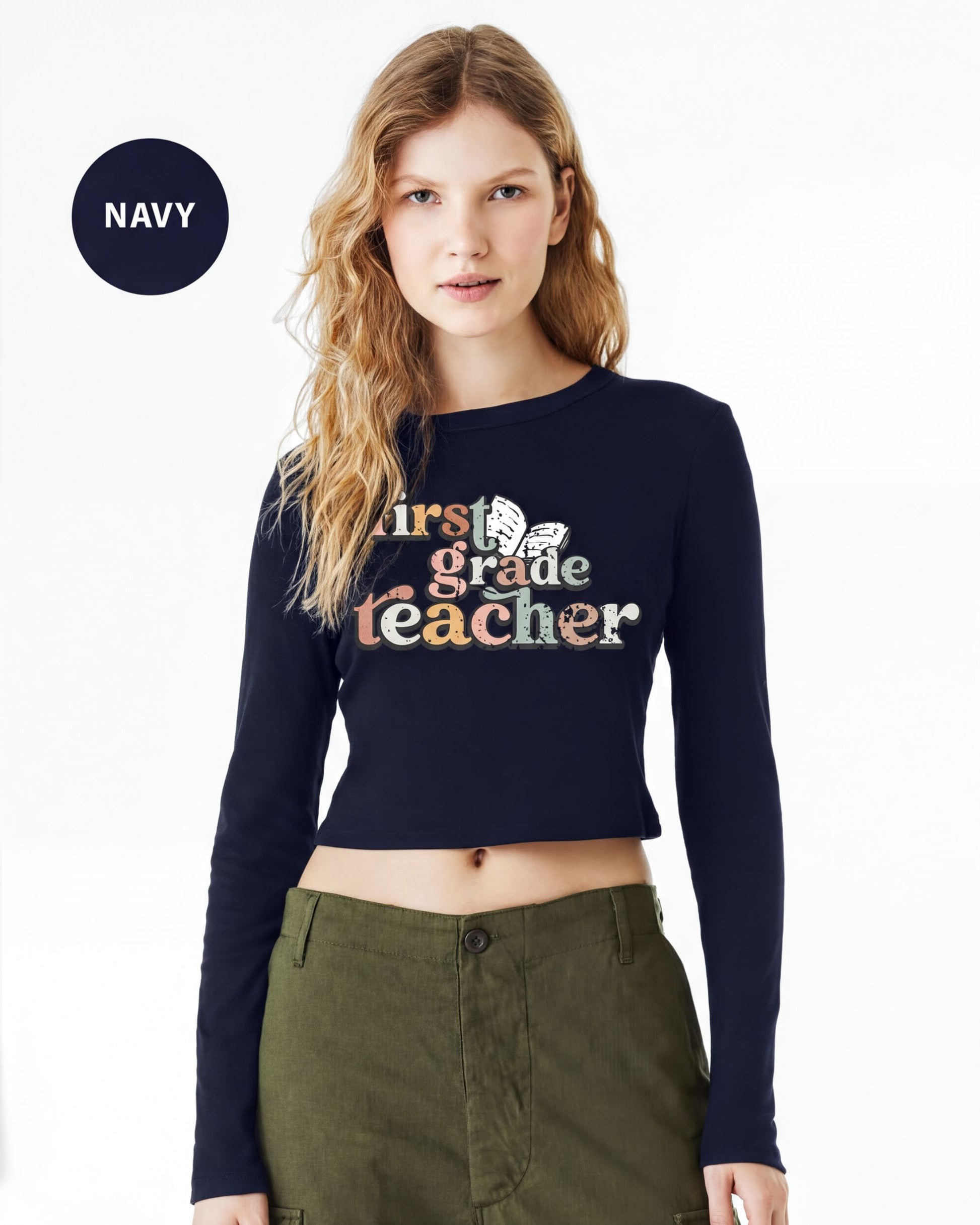 A woman wearing a navy blue crop top with the text "First Grade Teacher" printed on it, standing against a white background.