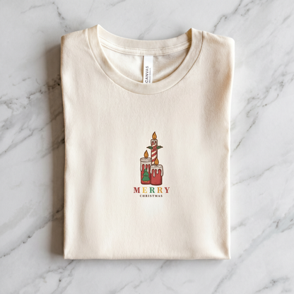 A white t-shirt with a graphic design of two candles and the text "MERRY CHRISTMAS" printed on it.