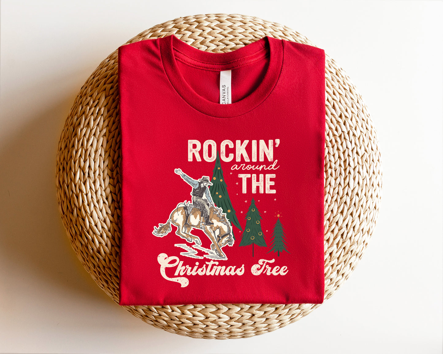 A red t-shirt with a graphic design depicting a cowboy on a horse, along with the text "ROCKIN' around THE CHRISTMAS Tree".