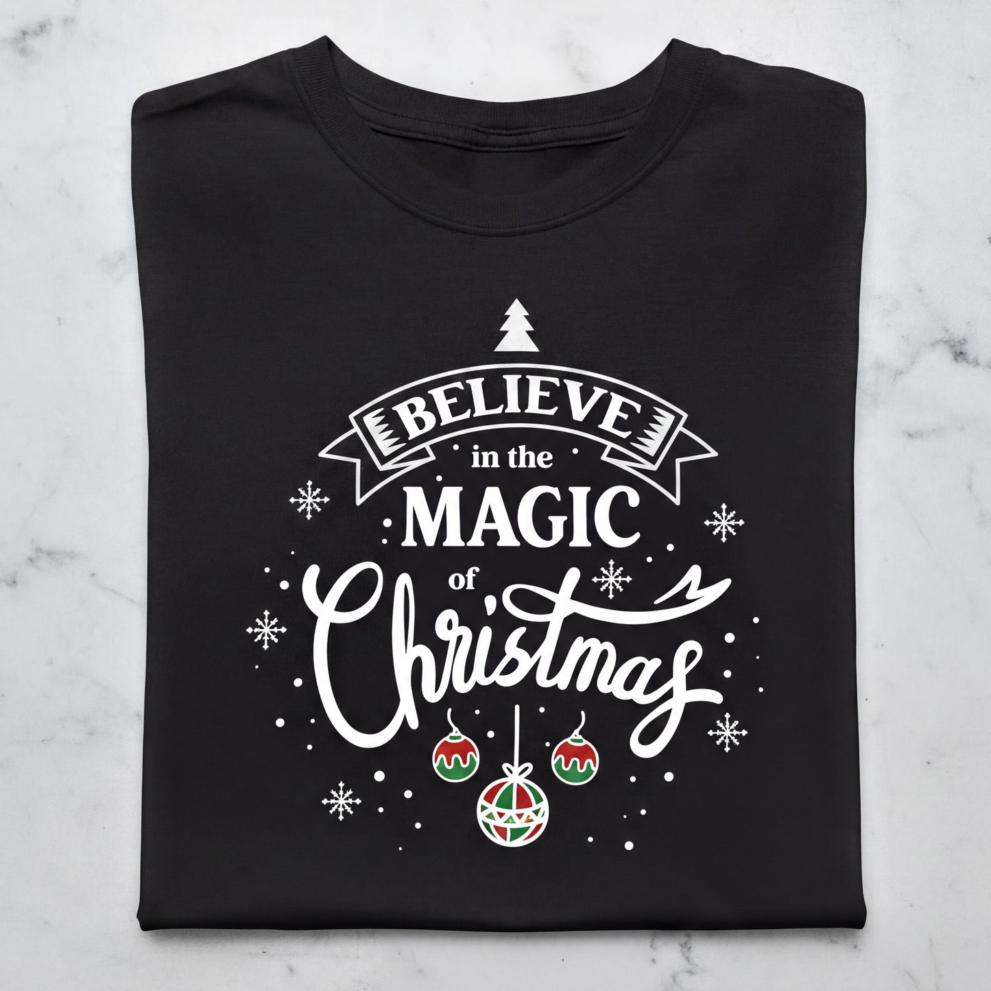 A black t-shirt with a white and red design featuring the text "Believe in the Magic of Christmas" and various Christmas-themed elements such as snowflakes, ornaments, and a small Christmas tree.