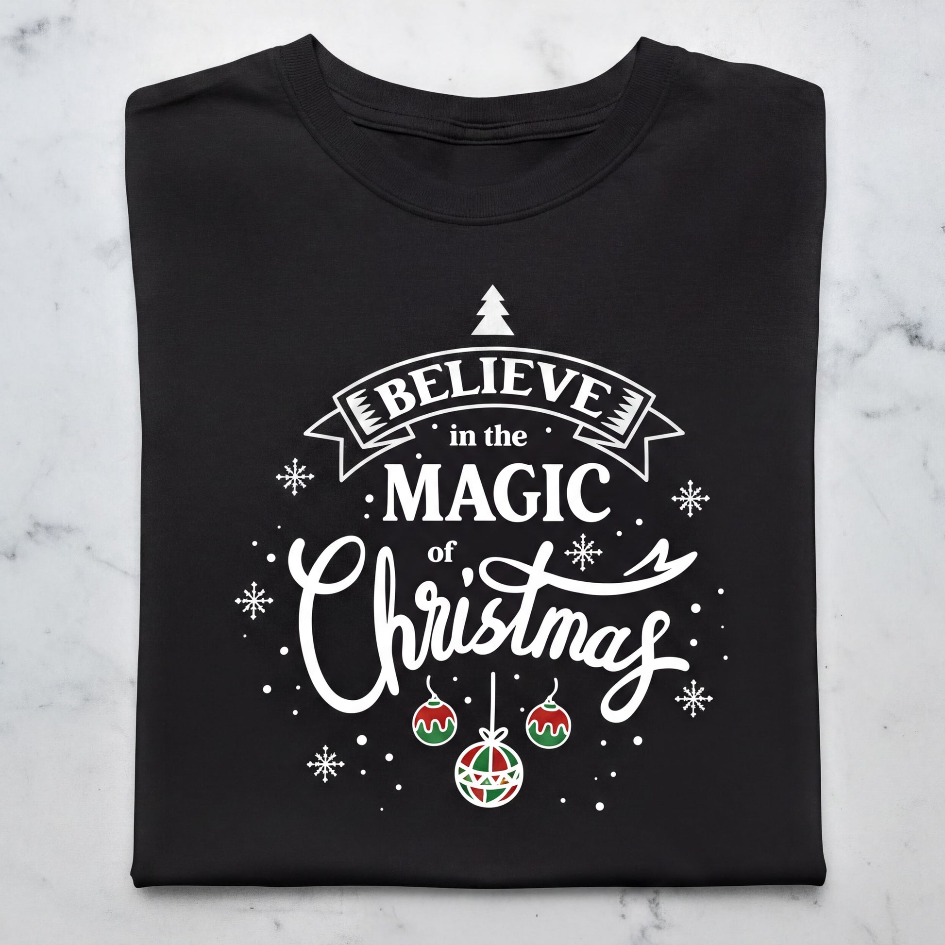 A black t-shirt with a white and red design featuring the text "Believe in the Magic of Christmas" and various Christmas-themed elements such as snowflakes, ornaments, and a small Christmas tree.