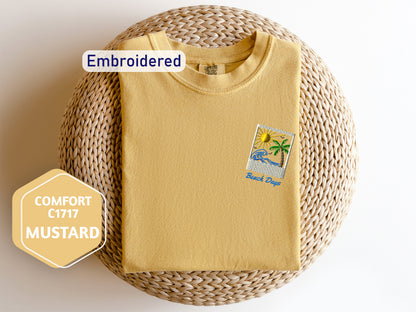 a yellow t-shirt with a beach-themed embroidered patch on the front, placed on a woven basket.