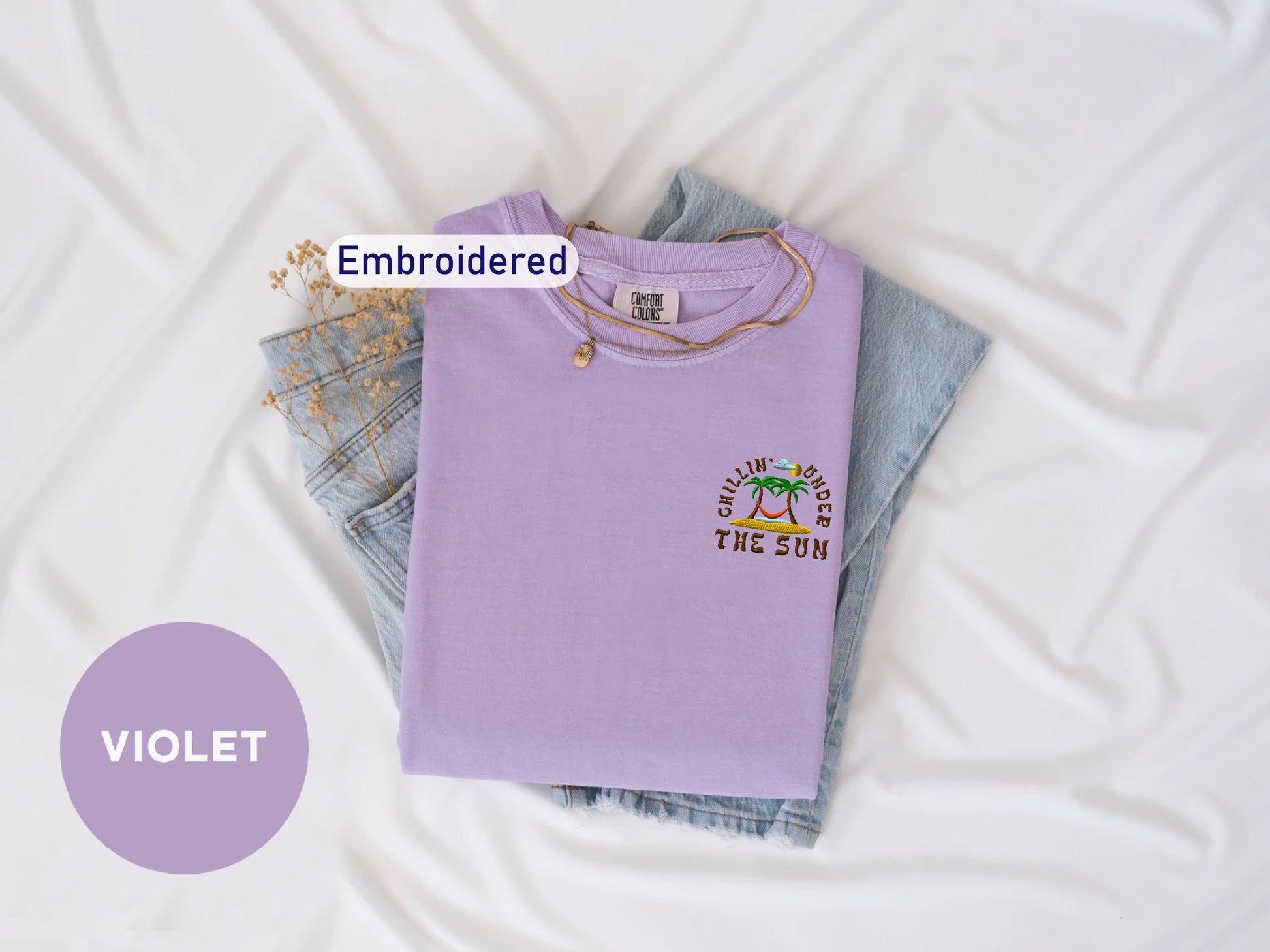 a purple t-shirt with a graphic design, a pair of denim jeans, and a necklace, all laid out on a white background.