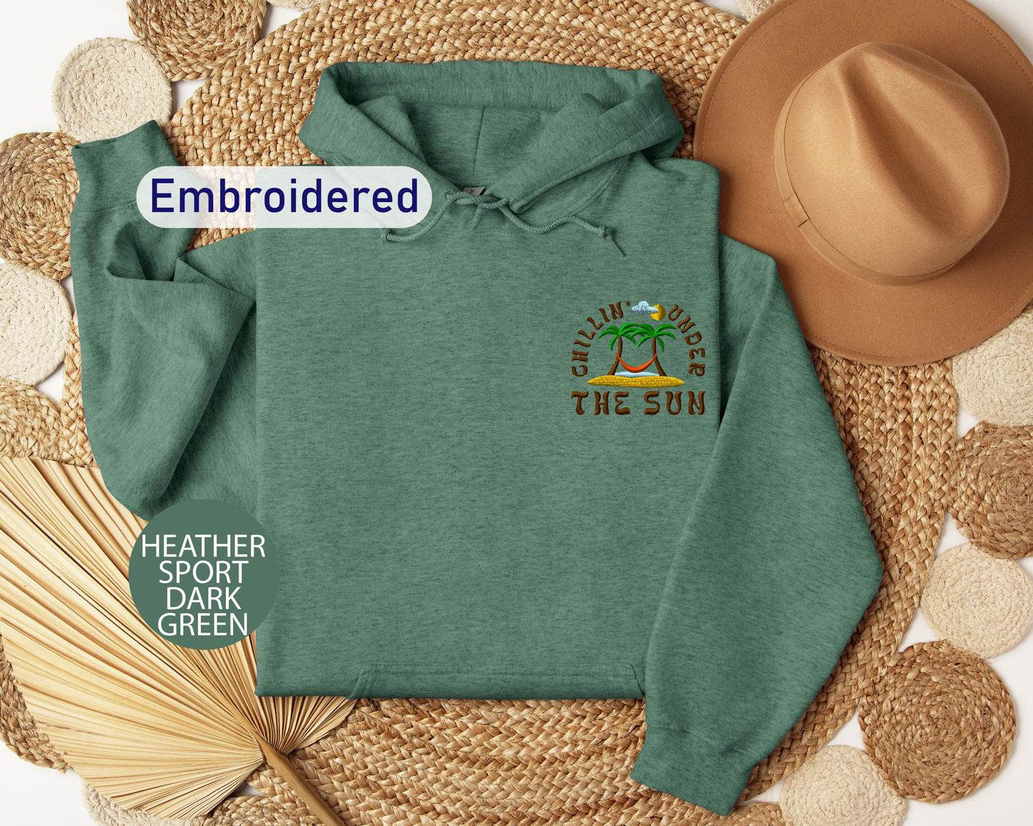 a green hoodie with a palm tree design, a brown hat, and a woven mat, all arranged on a white background.