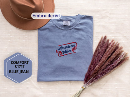a collection of clothing and accessories, including a blue t-shirt with an embroidered design, a brown hat, and a bunch of purple flowers.