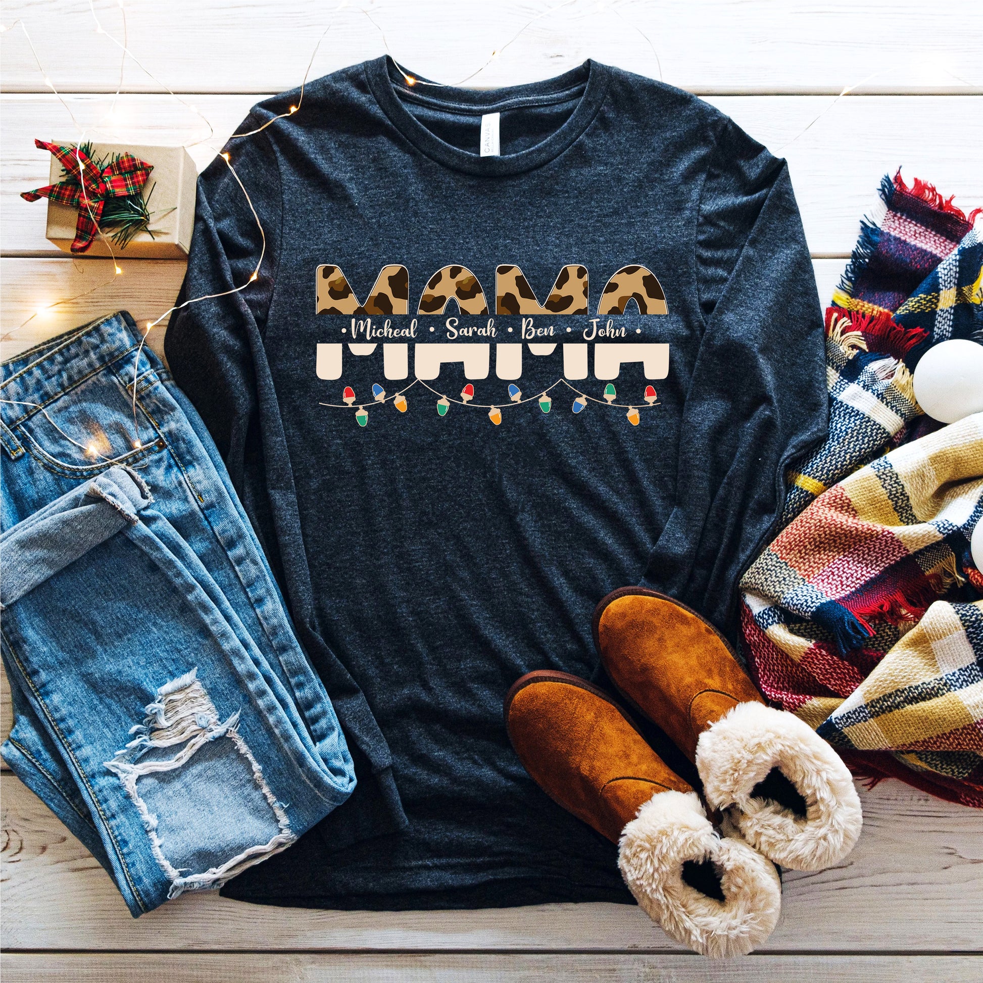A casual outfit consisting of a black long-sleeved shirt with a leopard print design, distressed blue jeans, brown boots, and a colorful plaid scarf is laid out on a wooden surface.