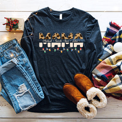 A casual outfit consisting of a black long-sleeved shirt with a leopard print design, distressed blue jeans, brown boots, and a colorful plaid scarf is laid out on a wooden surface.