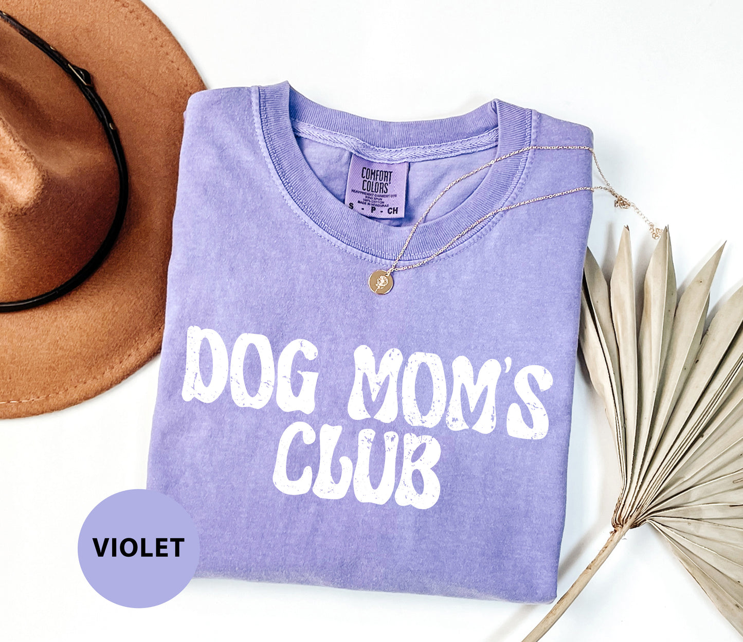 a purple shirt that says dog mom's club next to a hat