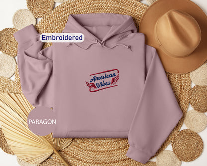 a gray hoodie with a red and blue embroidered logo, a brown hat, and a fan, all arranged on a woven mat.