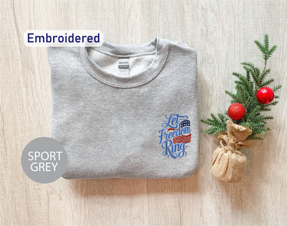 a grey sports sweatshirt with an embroidered design on the left chest area, along with a small Christmas tree and a burlap sack on the right side.